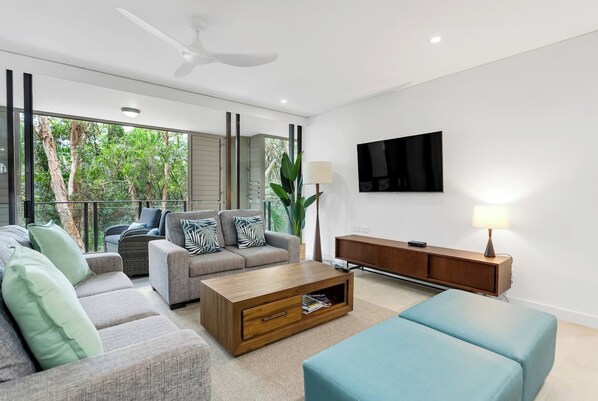 Stretch out in the inviting living area where contemporary comfort meets lush green surrounds, with natural light streaming through expansive sliding doors.