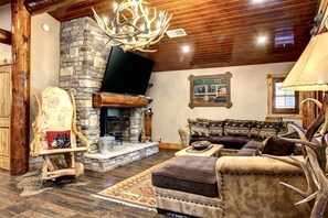 Living room features a cozy sectional, a massive Smart TV, & stone fireplace.