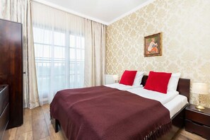 A cozy bedroom with a double bed covered in maroon bedding, accompanied by bedside tables and a decorative wall.

