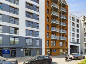 A modern apartment complex with sleek architecture and large glass windows, surrounded by parked cars.