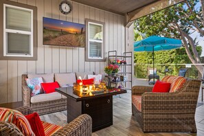 Covered outdoor entertainment room w/fire table, 55-inch TV, lounge seating.