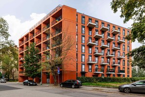 A striking orange apartment building surrounded by greenery and a paved walkway, with large windows and balconies visible.