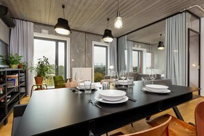 A long dining table set for multiple people, surrounded by contemporary chairs, with large windows in the background.