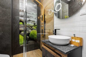 A bathroom with a walk-in shower, a modern vanity, and dark, earthy tile decor, combining functionality with style.