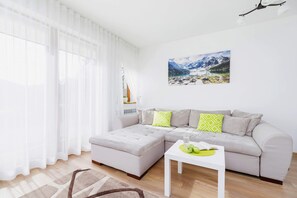A spacious living room with a gray sofa, a coffee table, and large windows allowing plenty of sunlight.