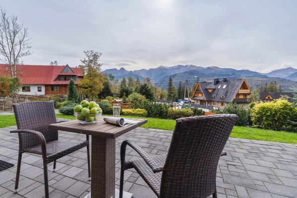  A table and chairs are arranged on a patio overlooking lush greenery and the mountains. Perfect for enjoying a meal outdoors.
