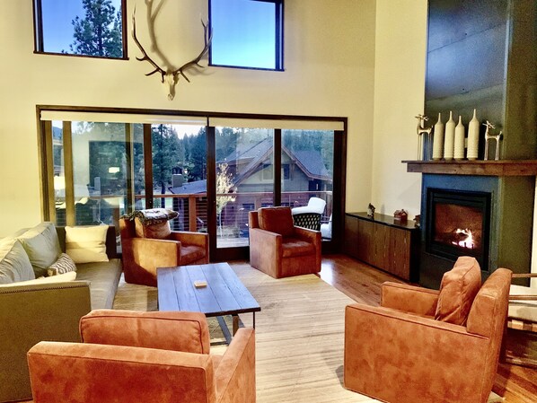 Large open great room with balcony, and 4 plush swivel chairs around fireplace. 