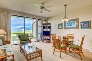 The bright and airy living room features tropical decor, cozy seating, and panoramic windows showcasing the outdoor beauty of Hawaii. NAP-B43