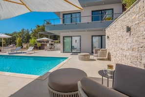 Outdoor terrace with seating with a small table, deckchairs for sunbathing and a heated swimming pool