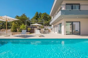 The outdoor heated swimming pool of the Croatia luxury villa Elegance in the town of MIlna on the island of Brac, surrounded by deckchairs for sunbathing in an umbrella