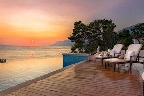 Sun deck with sunbeds next to a large heated swimming pool with a view of the sea next to the pebble beach of a modern family villa in Brela-Makarska, Croatia