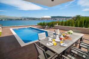 Covered part of the terrace with an outdoor dining table and private pool with sun loungers of a Croatia luxury holiday villa Trogir 1