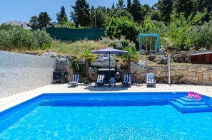 A spacious swimming pool with comfortable deckchairs and umbrellas and a view of the crystal blue sea from the property of a luxury villa for a family vacation on Korcula