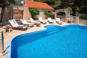 Exterior of a luxury Dalmatian stone villa in Bol on the island of Brac with a swimming pool, sundeck and garden next to pine trees