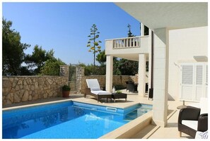 Private pool surrounded by sun loungers and sitting furniture in the fenced yard of the luxury villa by the beach in Primošten