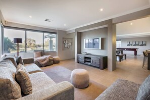 A spacious and inviting lounge with plush seating, a large TV, and floor-to-ceiling windows that frame the stunning outdoor scenery.