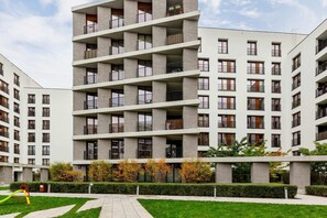 A view of a modern apartment building surrounded by a well-maintained courtyard. The architecture features clean lines and a neutral color palette.