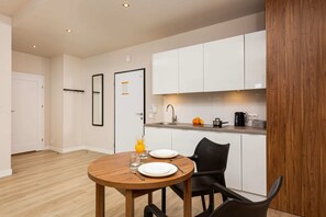  A sleek, minimalist kitchen with white cabinetry and wood accents. A small dining table with chairs is placed nearby for casual meals.