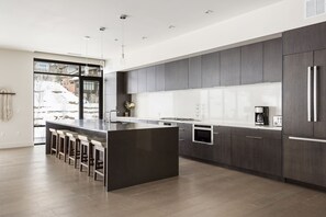 Stunning chef's kitchen with dark quartz kitchen island and barstool seating, white quartz countertops and backsplash, panel ready refrigerator and dark wood cabinetry