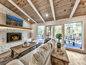 Welcome to the great room with a warm fireplace, 55' TV, and sliding glass doors to the expansive wrap-around deck