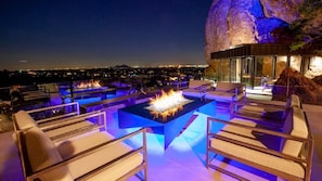 Modern patio with a fire pit, city views, and a dramatic rocky cliff backdrop.