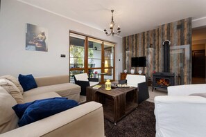 A spacious living room with a soft sofa, armchair and coffee table invites you to relax by the fireplace located next to a wall with wallpaper imitating tree bark.