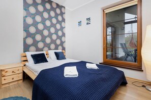 A cosy bedroom with a double wooden bed with white linen and a navy blue bedspread on which towels lie.