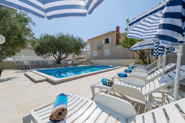 Private terrace of Podstrana luxury rental villa with pool surrounded by deckchairs and sunshade for family vacation