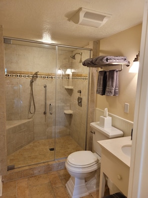 Spacious shower stall with seat, plush towels, and lighted magnifying mirror