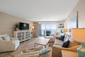 Living Room area includes a sleeper sofa, sitting chairs, and a large flat screen TV with cable. Door access to private balcony.