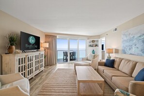 Living Room area includes a sleeper sofa, sitting chairs, and a large flat screen TV with cable. Door access to private balcony.