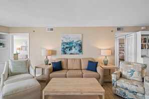 Living Room area includes a sleeper sofa, sitting chairs, and a large flat screen TV with cable. Door access to private balcony.