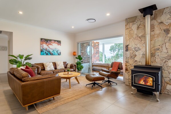 Cosy up in the stylish living room, complete with leather seating, a wood fire, and serene views of the treetops.