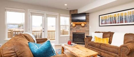 Experience the cozy living room, outfitted with plush seating, an expansive smart TV, fireplace, and patio doors that frame the breathtaking mountain vistas.