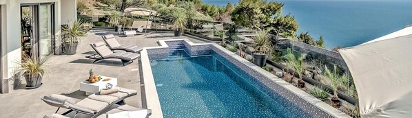 Spacious fenced terrace with private pool surrounded by sun loungers and seaview from the property of the luxury villa Happiness