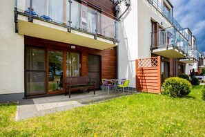 A grassy yard outside a house, with a patio featuring wooden paneling and garden furniture for relaxation.