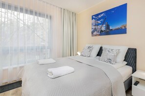 A stylish bedroom with a gray bed, white linens, and a large cityscape artwork on the wall, providing a calm and sophisticated atmosphere.