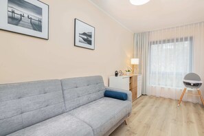 A comfortable gray sofa positioned near a large window with sheer curtains, complemented by minimalistic decor for a clean and airy look.