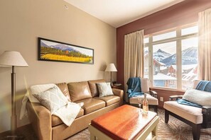 Sun-drenched living room with gas fireplace, deck with seating, and an incredible view of the Three Sisters and Rundle Mountain