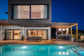 Outdoor dining table with chairs next to the private pool in front of the modern family villa for rent Indigo in Razanj and a BBQ with dining area