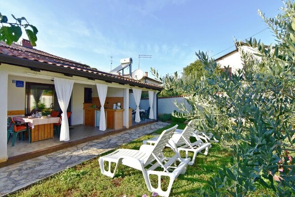 The exterior of the apartment with an equipped terrace and a large garden with deck chairs.