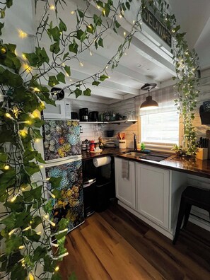 A warm and inviting kitchen with soft lighting and charming touches — lighted vines drape gently along open shelves, casting a cozy glow over rustic wood countertop
