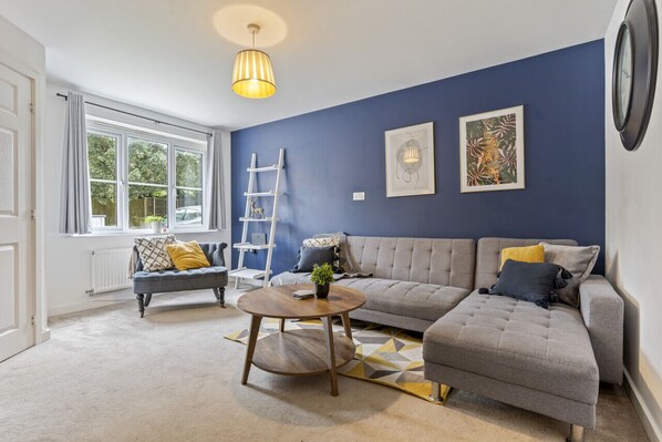 A cosy living room featuring a large corner sofa, arm chair and a 50'' Smart TV with Netflix subscription included