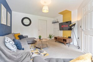 A cosy living room featuring a large corner sofa, arm chair and a 50'' Smart TV with Netflix subscription included