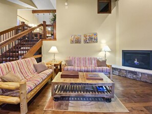 A living room with striped couches, a wooden coffee table, two table lamps, a fireplace, and a staircase in the background.