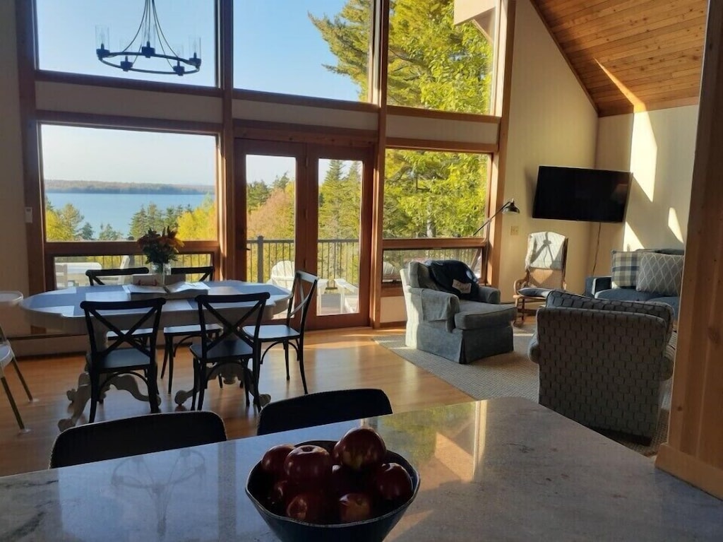 A living room with floor to ceiling windows offers an expansive view of the ocean and surrounding forest.