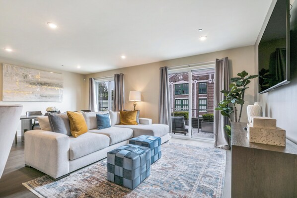 Side 1: Open-concept living, kitchen, and dining area with ample seating. Enjoy a 65” Samsung Smart 4K TV with streaming and DIRECTV Entertainment. Relax on the sofa and cozy chairs, dine at the table for six, and enjoy the natural light!