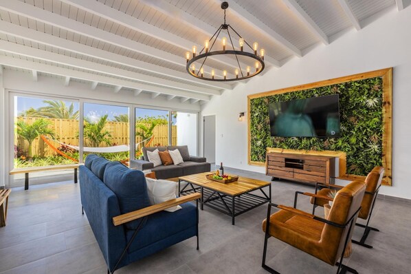 With its large comfortable sofa, Black wagon wheel chandelier, and a sustainable green wall on which the smart TV is hung, the living room area exudes a modern farmhouse rustic vibe.