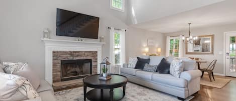 Living Room with fireplace, 65 inch smart TV and cathedral ceilings adjoins dining room.