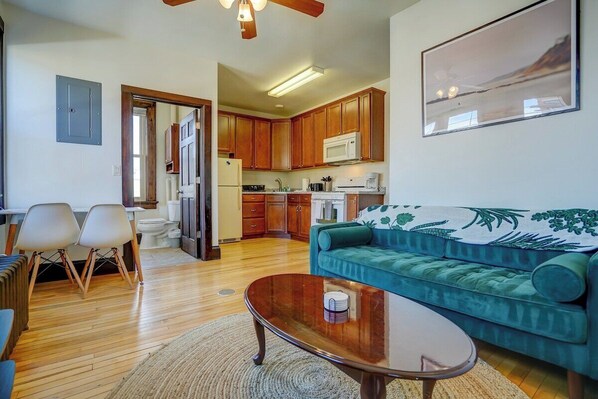 Living room with sofa, coffee table and workspace with view of kitchen in background.